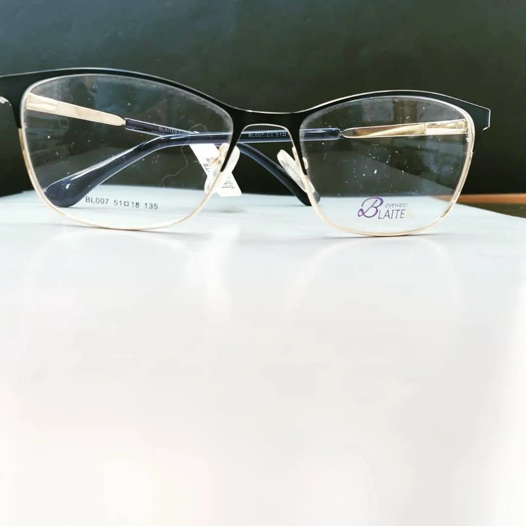 Black and gold soft-square glasses on a white table against a deep green wall