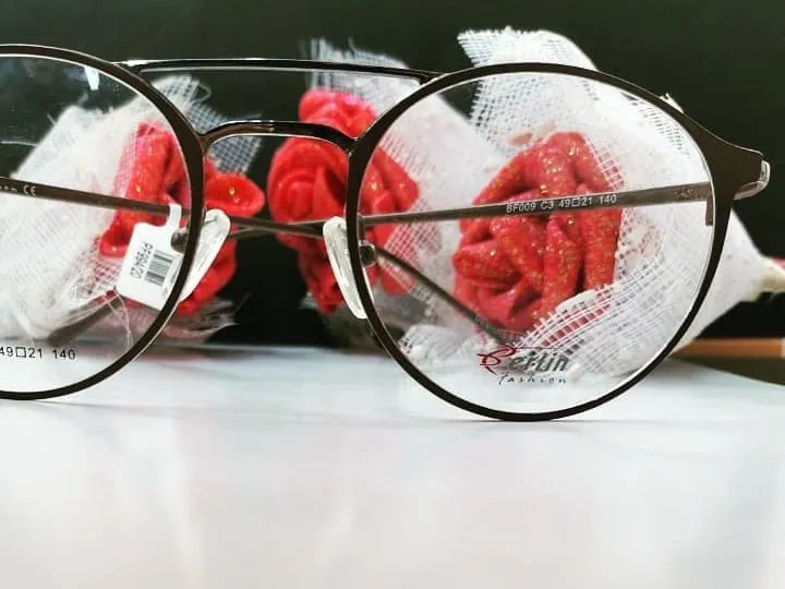 Round dark bronze glasses close up with red roses behind